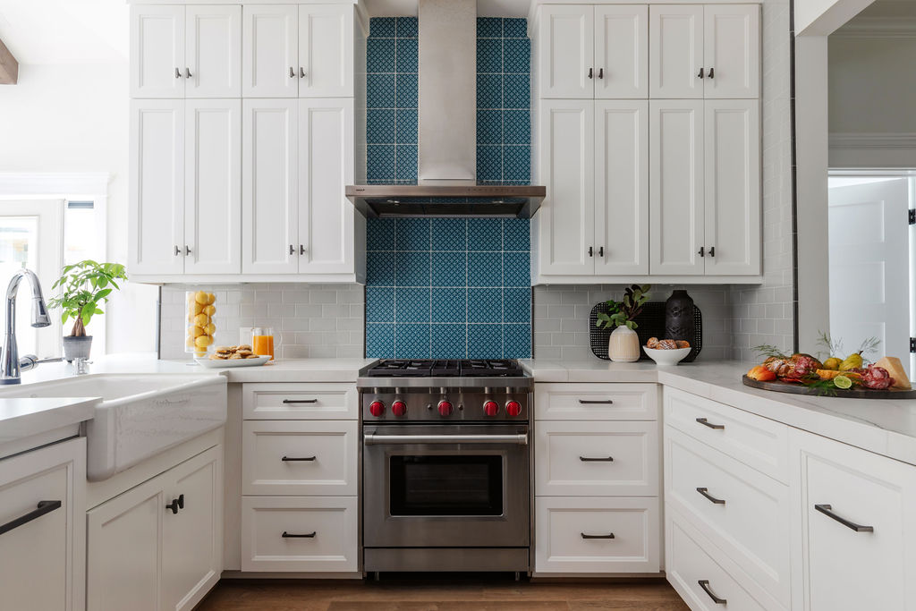 Bright, modern kitchen featuring Neolith Mont Blanc Silk countertops, white Shaker-style cabinetry, and a striking blue patterned tile backsplash behind a stainless steel Wolf gas range. Accents include a farmhouse sink, black hardware, and warm wood flooring. A Keechi Creek Builders Taft Project renovation in Houston Heights.