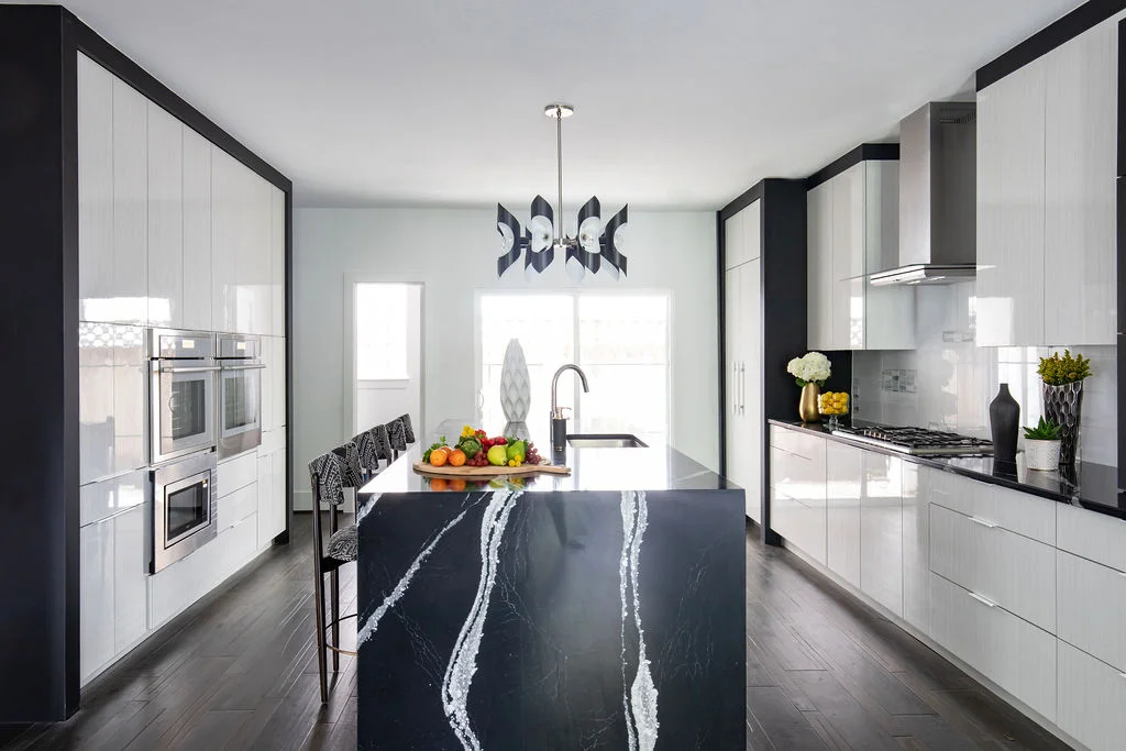 Modern luxury kitchen with a striking black island featuring white veining, sleek white cabinetry, built-in stainless steel appliances, and dark wood flooring, accented with contemporary lighting and decorative elements